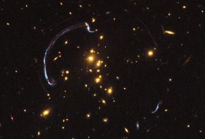Bright yellow-white galaxies against the black backdrop of space.. Faint streaks and arcs of gravitationally lensed background galaxies.